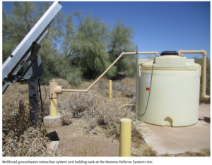 A big watertank is shown next to a solarpanel and some shrubs. Text on the image reads "Wellhead groundwater extraction system and holding tank at the Nammo Defense Systems site".